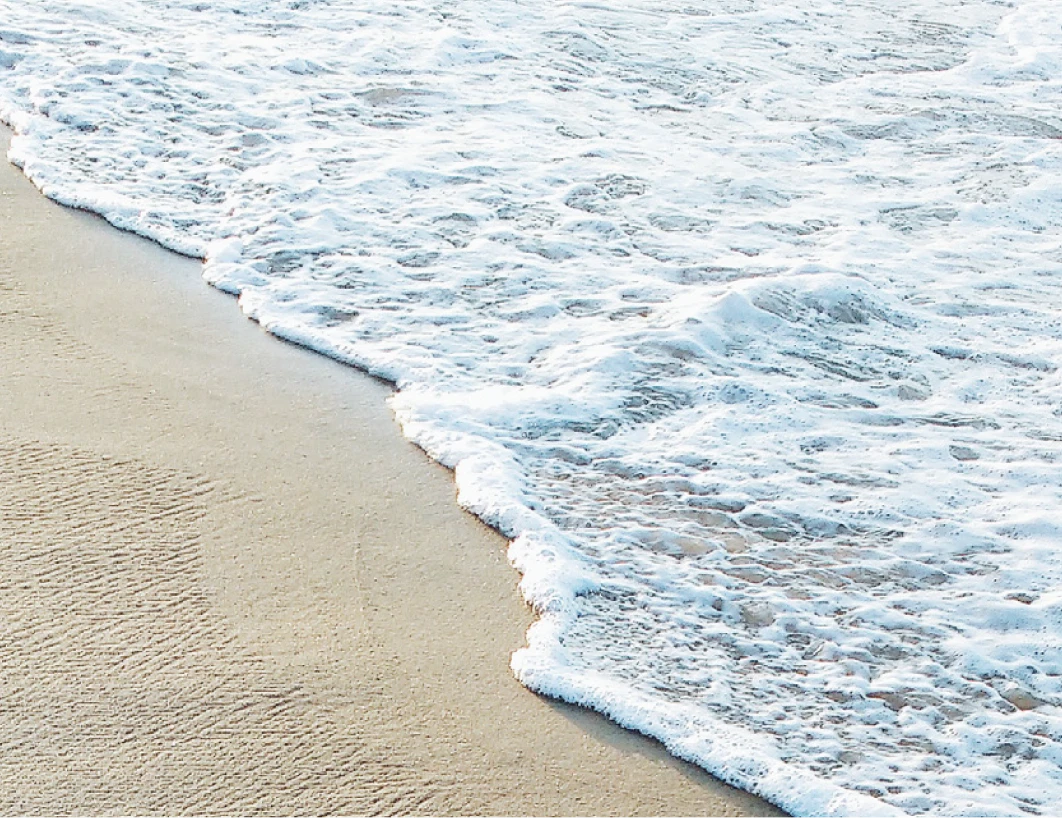 A serene beach scene featuring gentle waves lapping against golden sand under a clear blue sky.